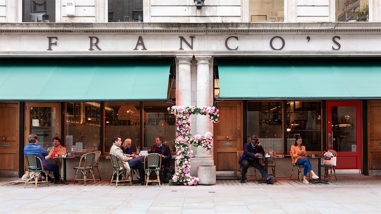People dining at tables under green awnings at Franco’s, beneath letters reading "Franco’s"